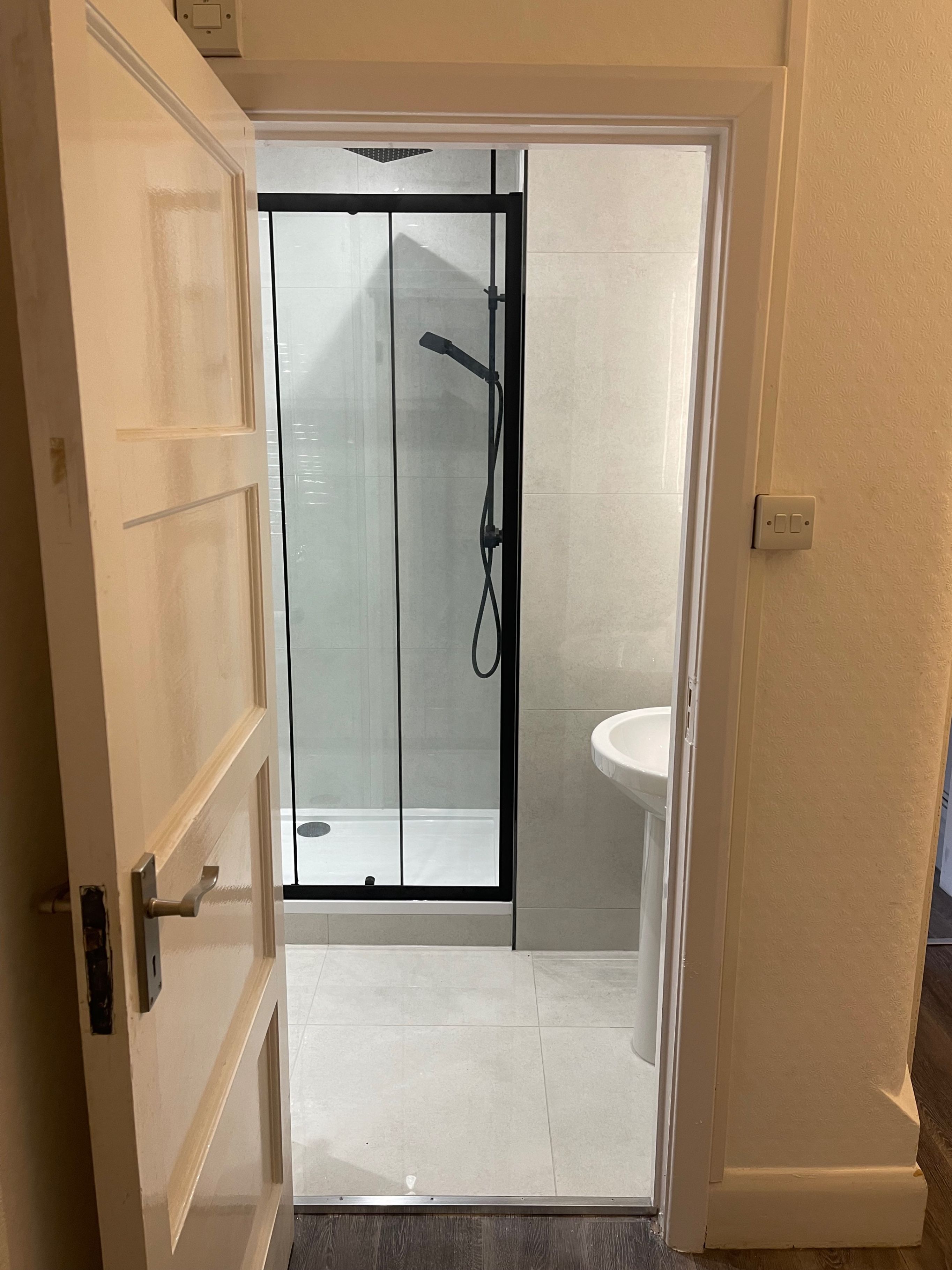 Un bagno con doccia vetrata, lavandino bianco e porta che conduce in un'altra stanza.