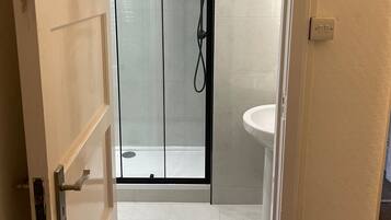 Un bagno con doccia vetrata, lavandino bianco e porta che conduce in un'altra stanza.