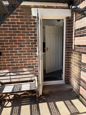 A narrow entrance to a building with a white door, a brick wall, and a wooden bench outside.