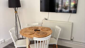 A dining area with a round table, white chairs, a floor lamp, and a mounted TV.