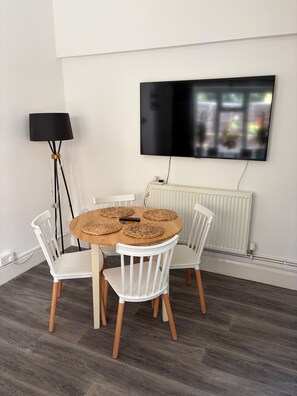A dining area with a round table, white chairs, a floor lamp, and a mounted TV. - 2-bed, Sleeps 4, Free Parking, Pets Allowed (Eastbourne)