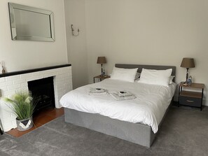 A neatly arranged bedroom with a bed, two bedside tables, a mirror, a fireplace, and a small plant.