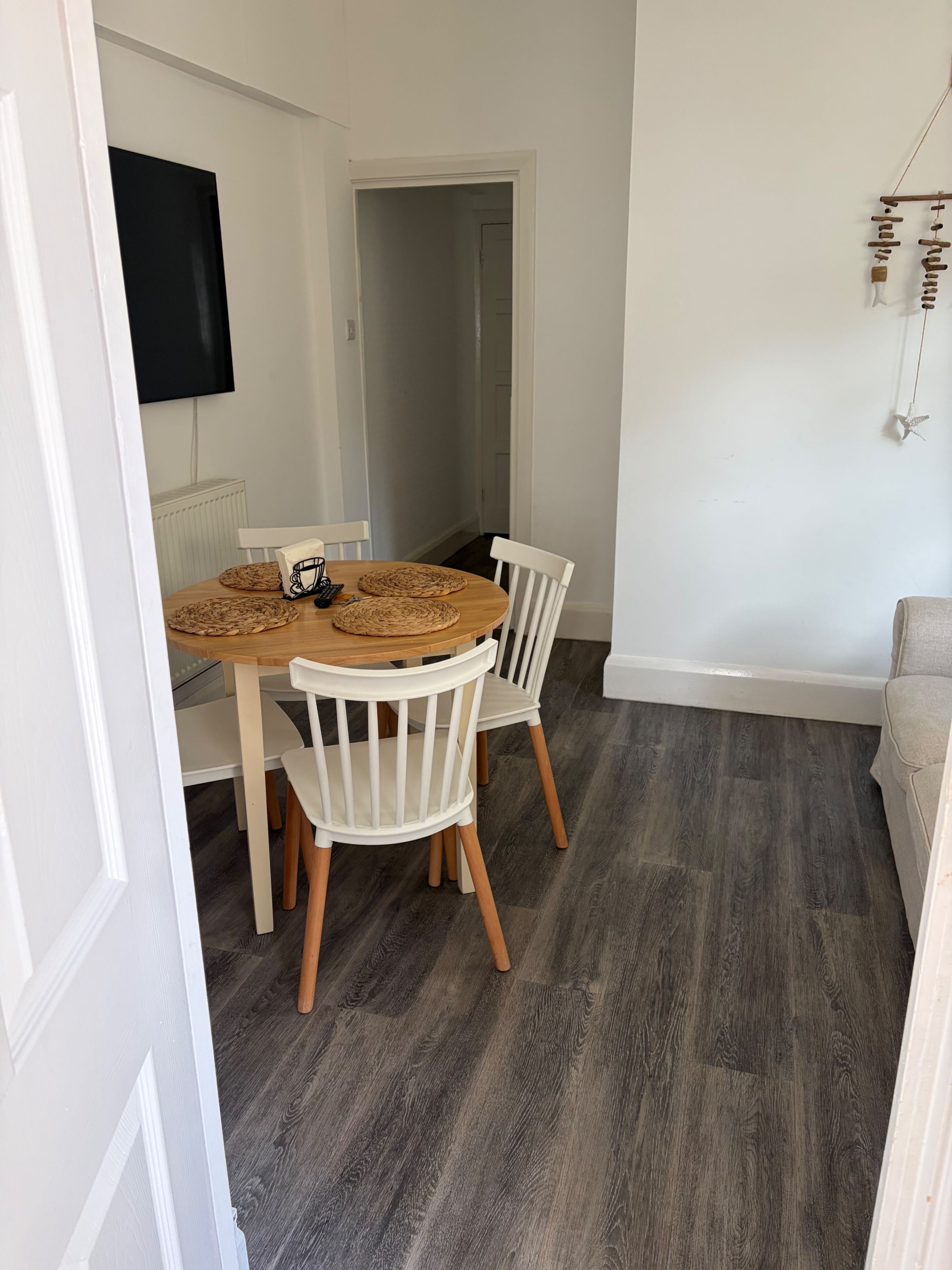 A dining area with a round table, white chairs, and a dark wooden floor.