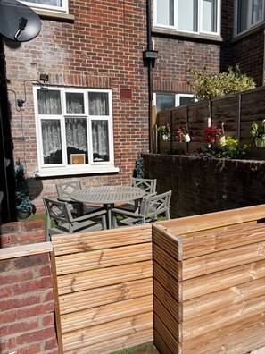 A brick house with a window, a satellite dish, and a wooden fence with potted plants. - 2-bed, Sleeps 4, Free Parking, Pets Allowed (Eastbourne)