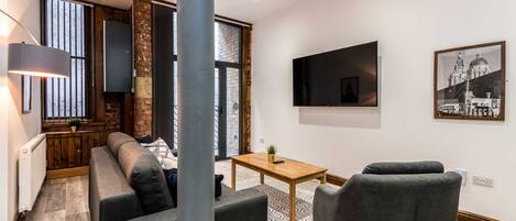 A modern living room with a sofa, armchairs, a coffee table, and a TV mounted on the wall.