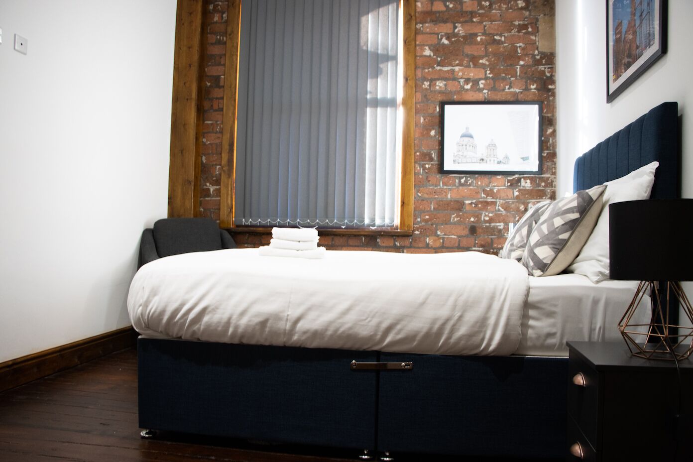 Un dormitorio con cama, mesita de noche, lámpara y ventana con persianas.