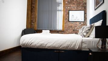 Un dormitorio con cama, mesita de noche, lámpara y ventana con persianas.