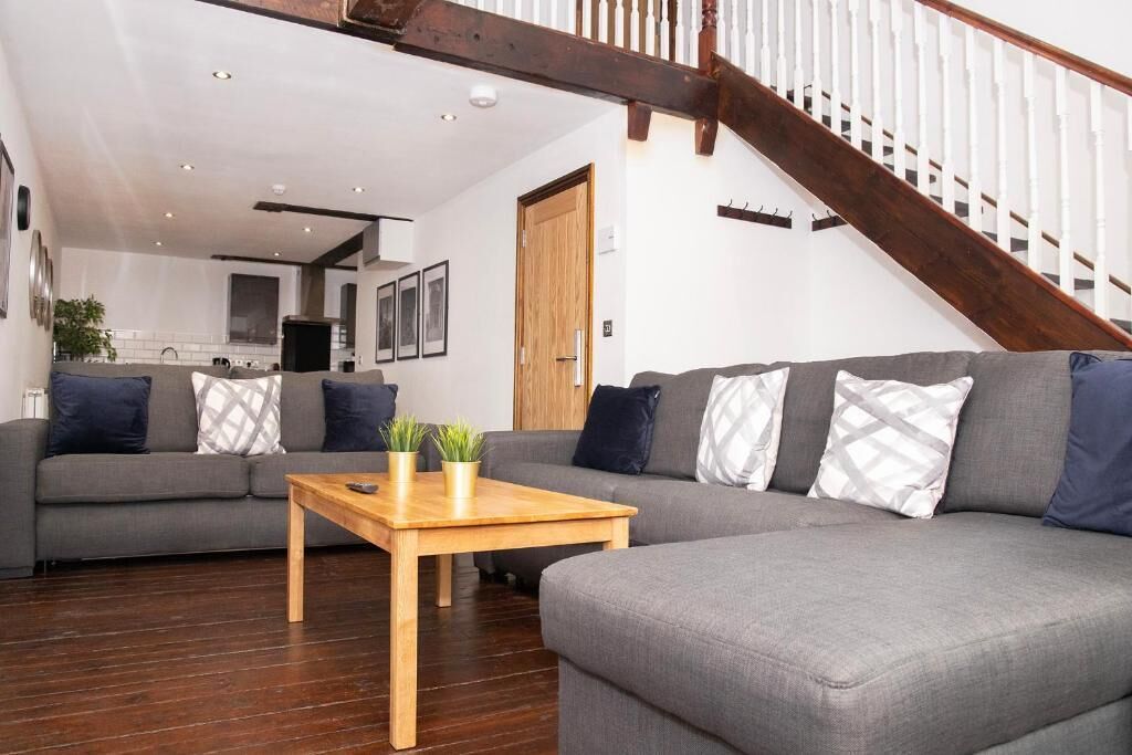 A modern living room with a grey sofa, wooden coffee table, and a staircase with white railings.