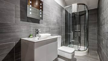 A modern bathroom with a glass-enclosed shower, a white sink, and a mirror with lights.