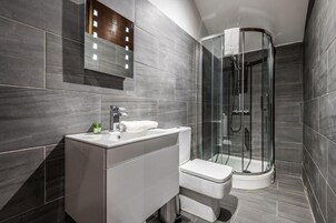A modern bathroom with a glass-enclosed shower, a white sink, and a mirror with lights.