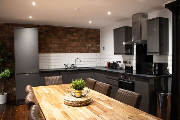 A modern kitchen with a wooden dining table, black cabinets, and a brick wall. - UStay 27 Stanley Street Party Apartments (Liverpool)