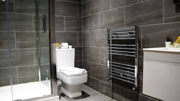 A modern bathroom with a glass shower enclosure, a white toilet, and a chrome towel rack.
