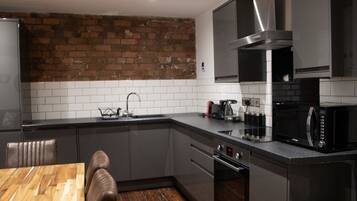 A modern kitchen with grey cabinets, a brick wall, a stainless steel range hood, a microwave, and a coffee maker.