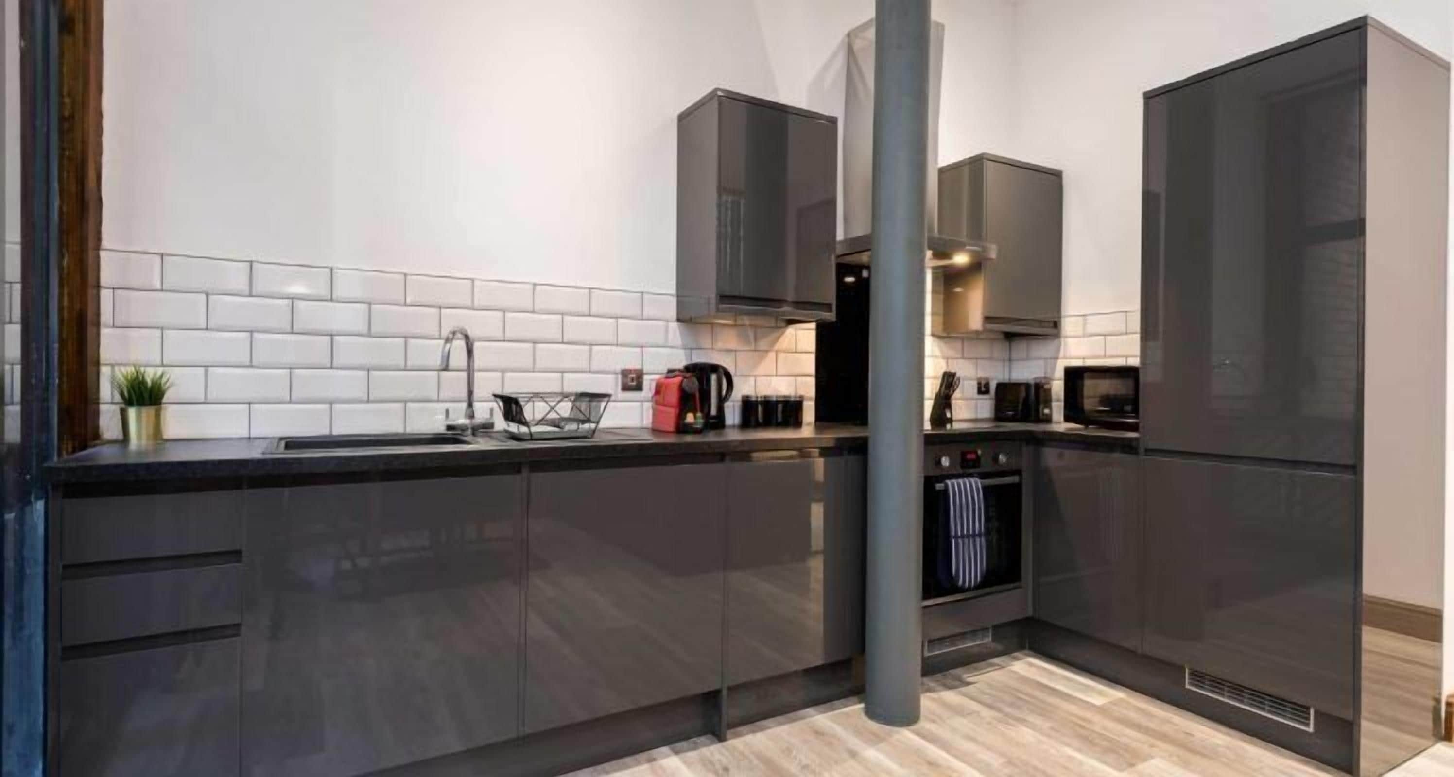 Una cocina moderna con armarios oscuros, un lavamanos de acero inoxidable y un horno empotrado.