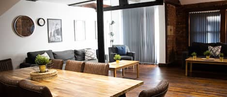 Ein geräumiger Wohnbereich mit Esstisch aus Holz, Ledersofas und einem großen Fenster mit Vorhängen.