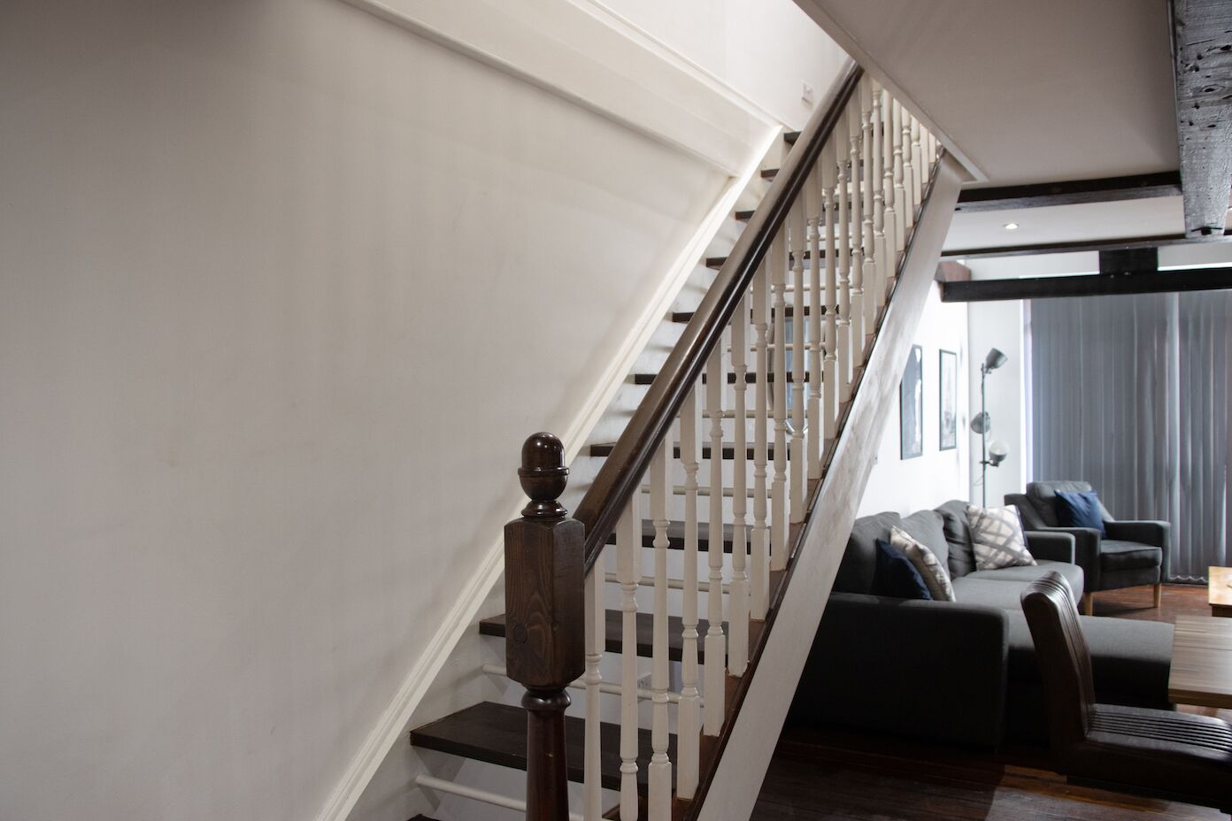 Una escalera moderna con barandillas de madera y una barandilla oscura, que lleva a una sala de estar con un sofá de color oscuro y una mesa de centro.