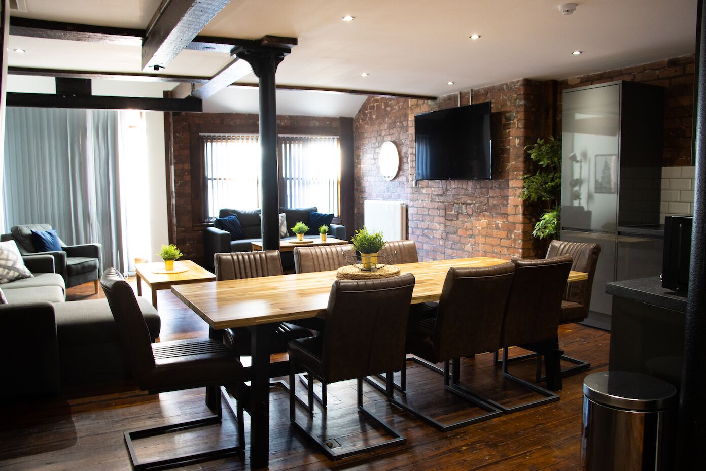 A modern living room with a wooden dining table, leather chairs, and a brick wall.