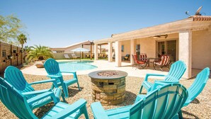 Ein Poolbereich mit blauen Adirondack-Stühlen, einer Steinkaminfeuerstelle und einer überdachten Terrasse mit Liegestühlen.