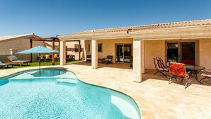 Ein Schwimmbecken mit Liegestühlen, einem Tisch mit Stühlen und einer überdachten Terrasse.