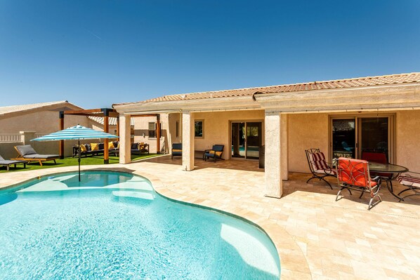 A swimming pool with lounge chairs, a table with chairs, and a covered patio area.