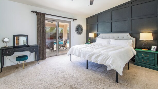 Ein Schlafzimmer mit Bett, Schreibtisch, Stuhl, Nachttisch, Lampe, Deckenventilator und Blick durch eine Glastür.