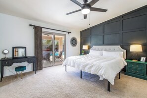 A bedroom with a bed, a desk, a chair, a nightstand, a lamp, a ceiling fan, and a view through a glass door.