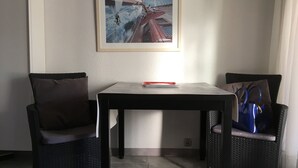Un coin repas avec une table et deux chaises, un tableau encadré au mur et un sac bleu posé sur une chaise.
