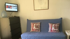 Une pièce avec un canapé bleu matelassé, deux coussins décoratifs, un téléviseur posé sur un meuble et un tableau encadré accroché au mur.
