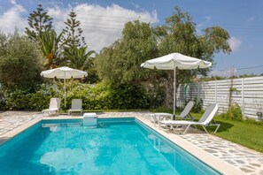 A swimming pool with lounge chairs and umbrellas, surrounded by greenery and a white fence. - Michaelo Villa - Affordable Luxury - Michaelo Villa - Affordable Luxury (Zakynthos)