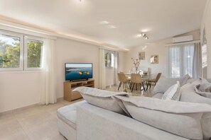 A modern living room with a large sofa, a TV, and a dining area. - Michaelo Villa - Affordable Luxury - Michaelo Villa - Affordable Luxury (Zakynthos)