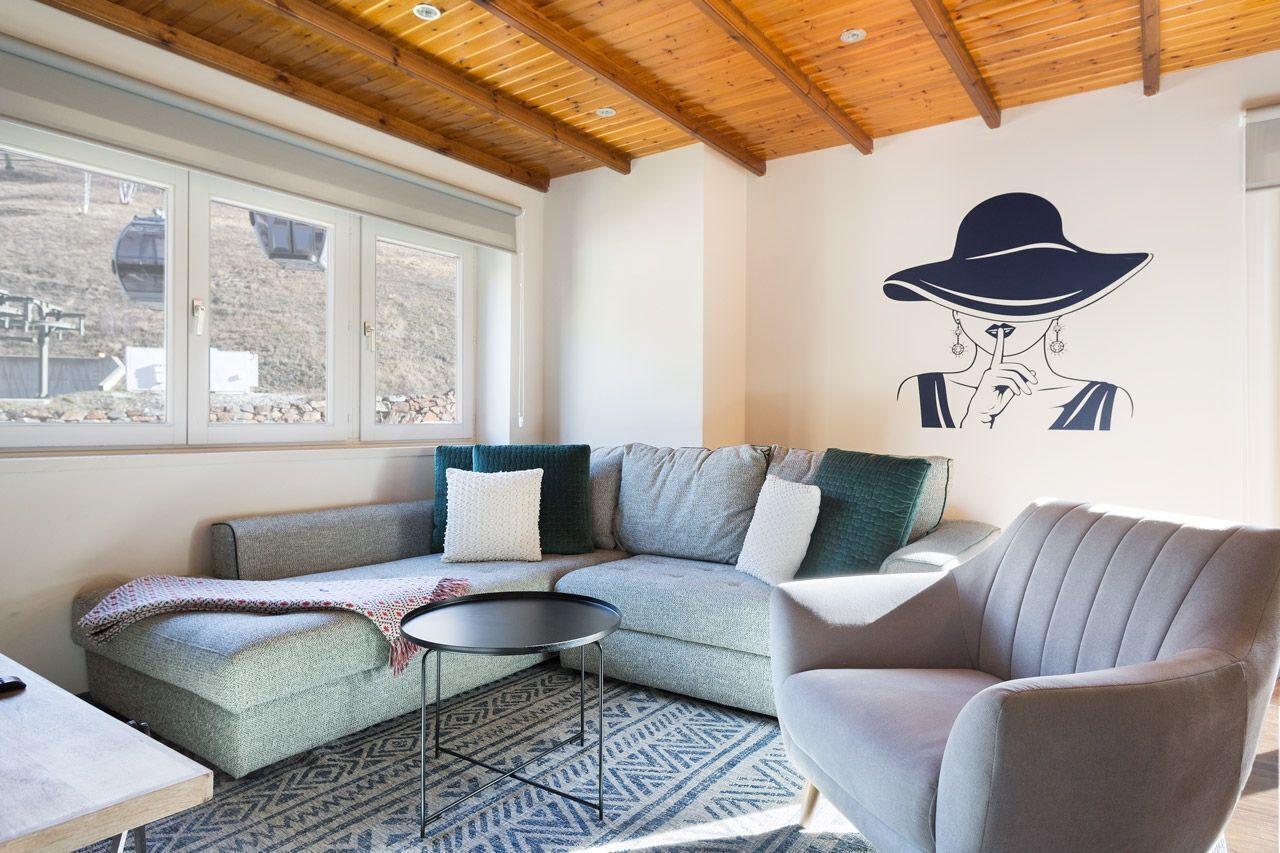 Una sala de estar acogedora con un sofá modular, una mesa redonda de centro y un ventanal con vistas a un paisaje montañoso.
