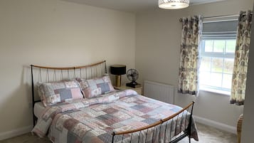Une chambre à coucher avec un lit, une table de chevet, une lampe, un radiateur et une fenêtre avec des rideaux.
