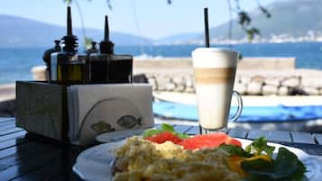 A breakfast setting with scrambled eggs, toast, and a drink, overlooking a coastal view with a pool and mountains in the background.