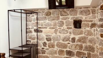 A room with a stone wall, a television mounted above it, and a bed with a wooden headboard.