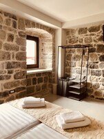 Un dormitorio con paredes de piedra, una ventana, una cama con toallas y una estantería de metal.