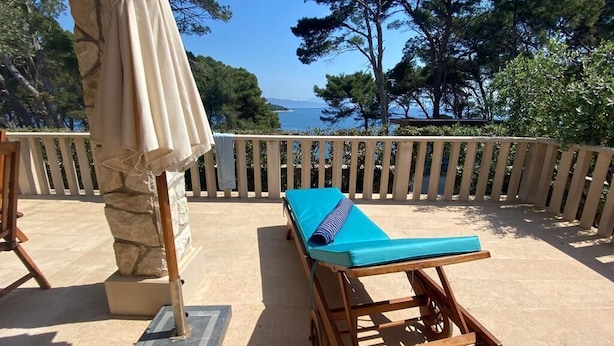 A wooden lounge chair with a blue cushion on a balcony overlooking the sea.