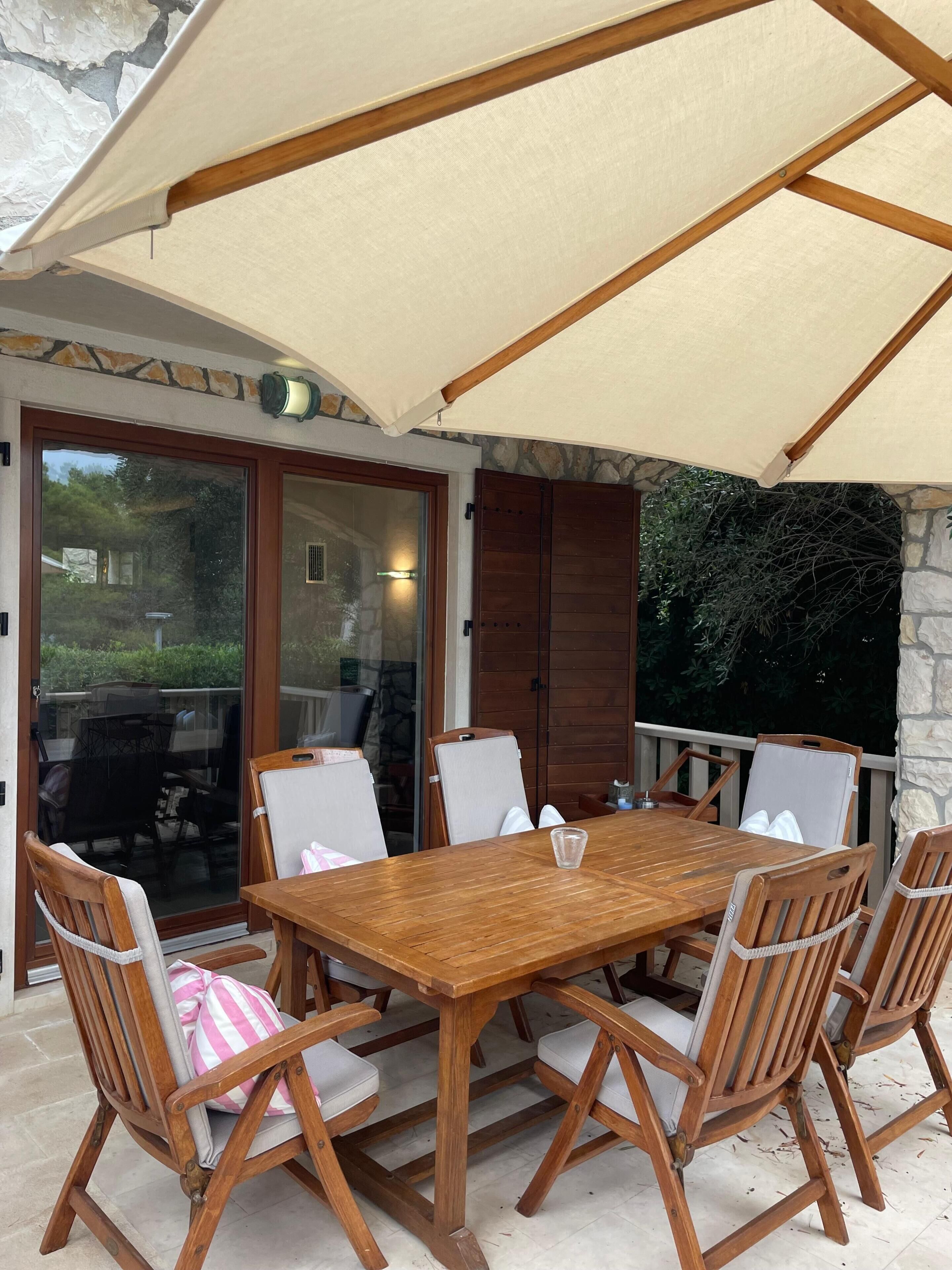 An outdoor patio with a wooden table and chairs, a large canopy, and a stone wall.