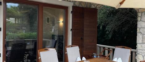 An outdoor patio with a wooden table and chairs, a large canopy, and a stone wall.