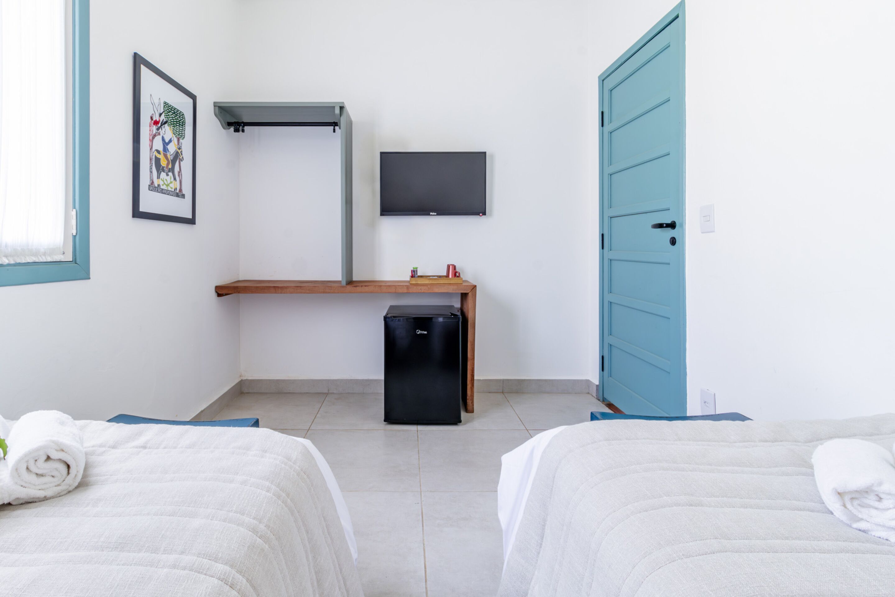 Quarto de hotel com duas camas, uma pequena mesa, uma televisão e uma porta azul.