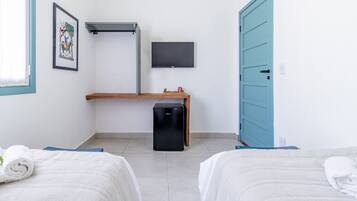 Quarto de hotel com duas camas, uma pequena mesa, uma televisão e uma porta azul.