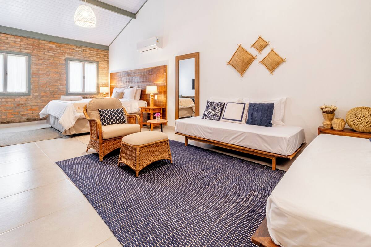 A spacious room with a large bed, a sitting area with a wicker chair, and a small table with a lamp.