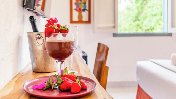 A dining table with a glass of red wine, strawberries, and a red plate.
