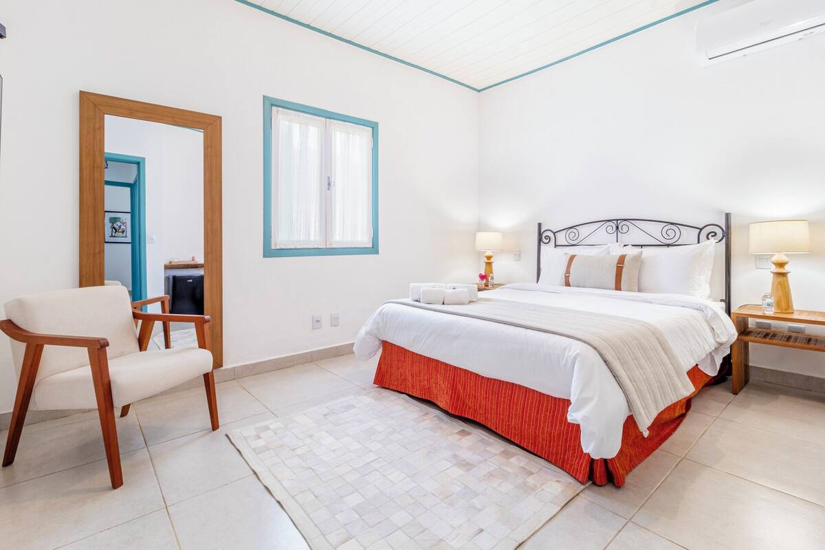 A bedroom with a bed, bedside tables, a chair, a mirror, and a window with curtains.