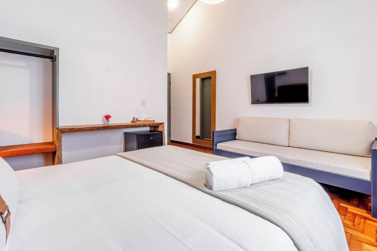 A hotel room with a bed, a sofa, a small desk, a mirror, and a TV.