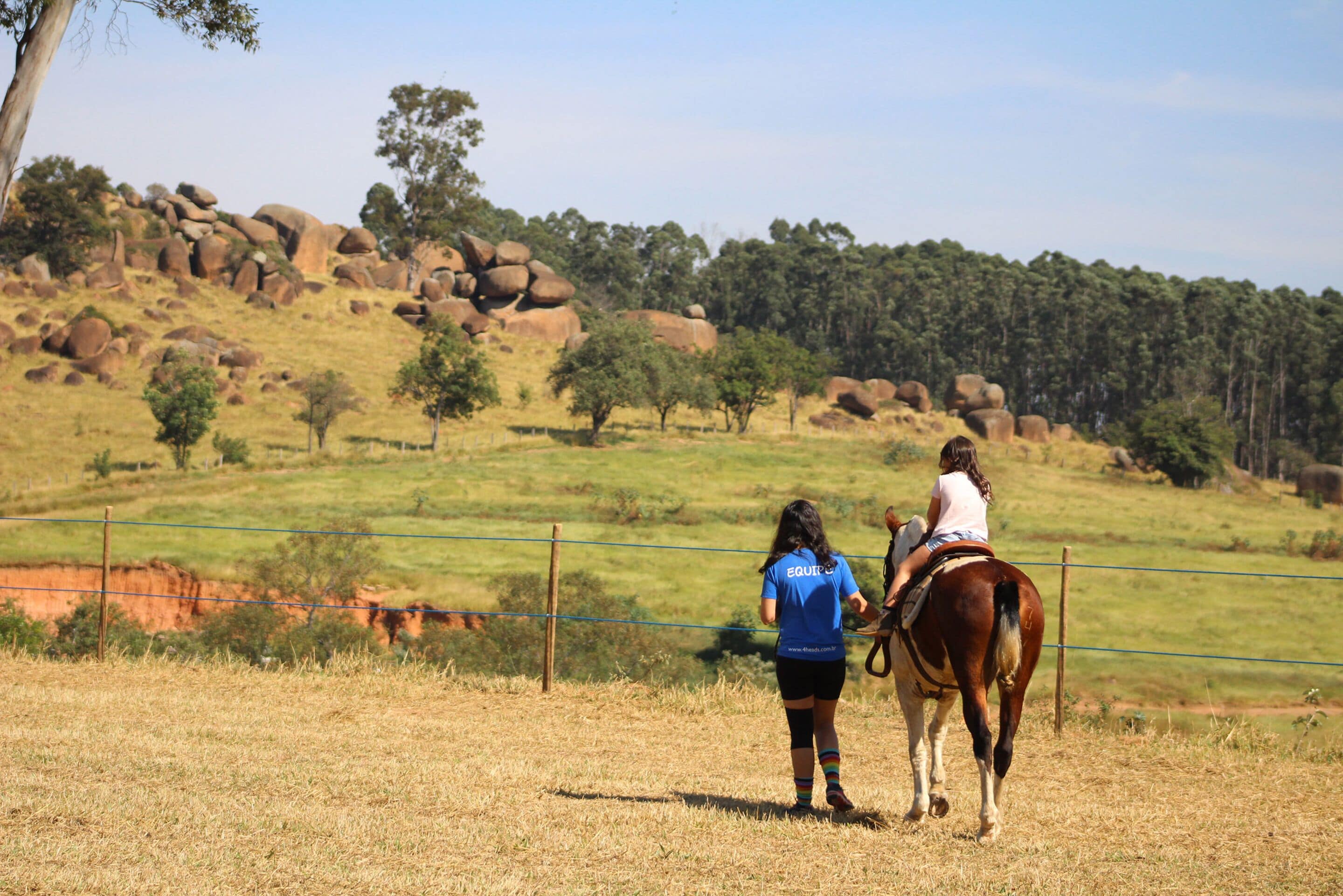 Una persona monta a caballo en un campo cercado con un paisaje montañoso al fondo.