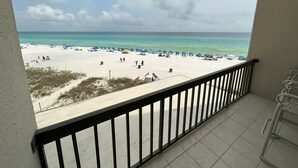 A balcony with a view of a beach with umbrellas and people.