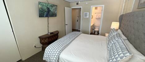 A hotel room with a large bed, a ceiling fan, a TV mounted on the wall, and a bathroom visible through an open door.