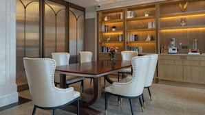 Un coin repas avec une table en bois et des chaises à revêtement blanc, entouré d’étagères remplies d’objets décoratifs.