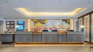 Un espace d’accueil d’hôtel au design moderne, comprenant un comptoir d’accueil, une grande fresque murale et un sol poli.