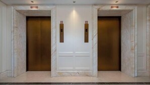 Une paire de portes d’ascenseur, avec un sol en marbre et un luminaire fixé au mur au-dessus.